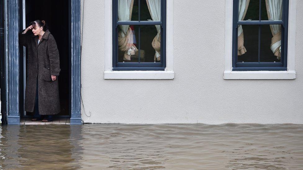 A resident of York stands on her doorstep beside a flooded street
