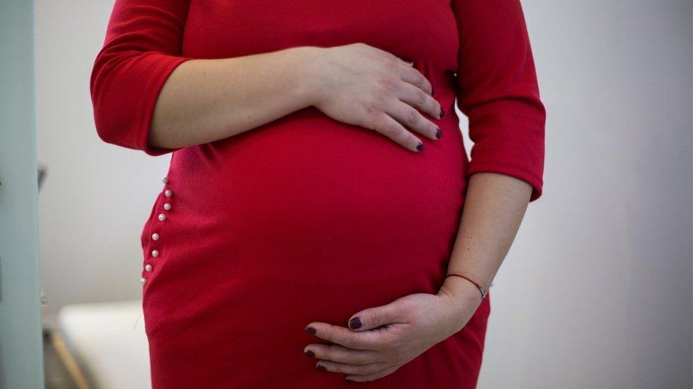 Tetiana, a surrogate, stands with her hands on her stomach. She is visibly pregnant.