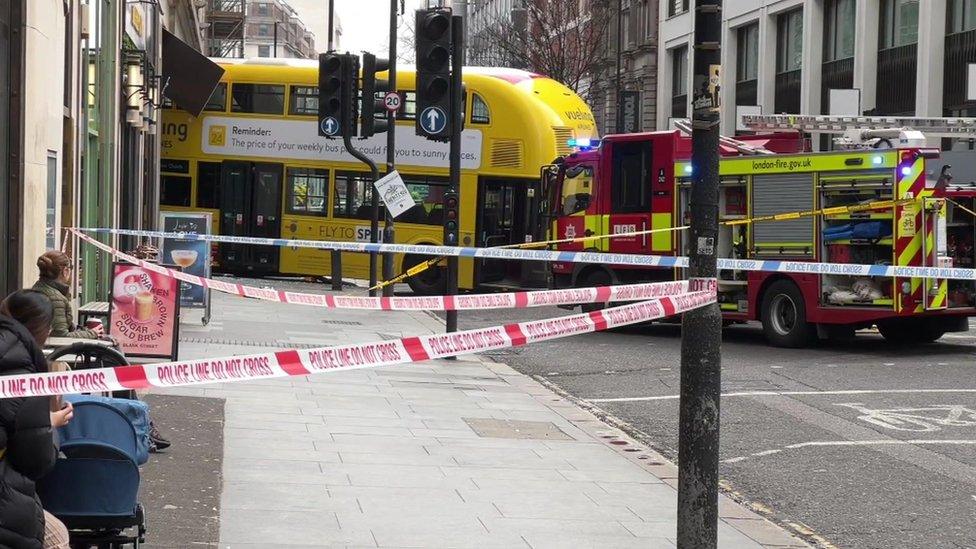 An image showing coffee shop customers looking on inside a cordon, with a fire engine parked to the right of the yellow bus