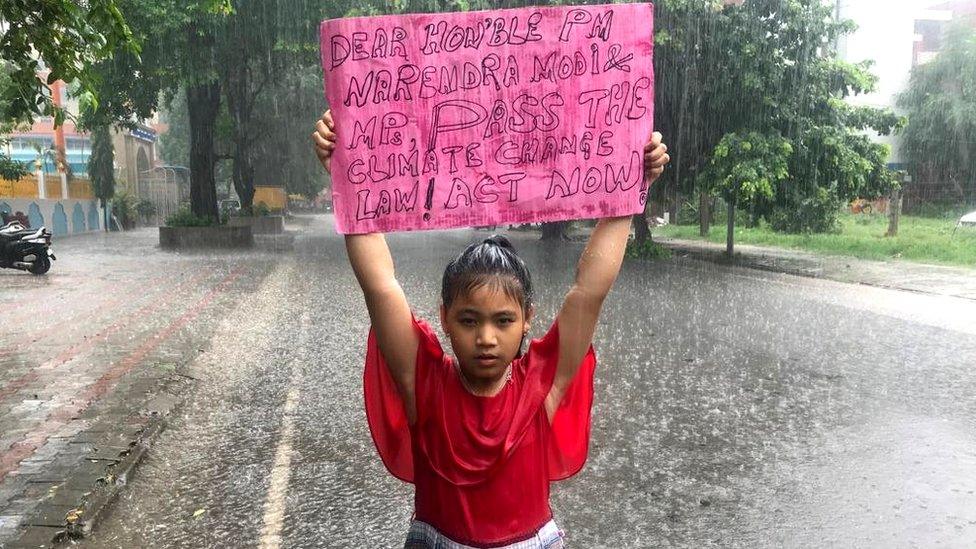 Licypriya Kangujam, eight, stands in the rain holding a sign urging the Indian government to pass a law on climate change, 2019