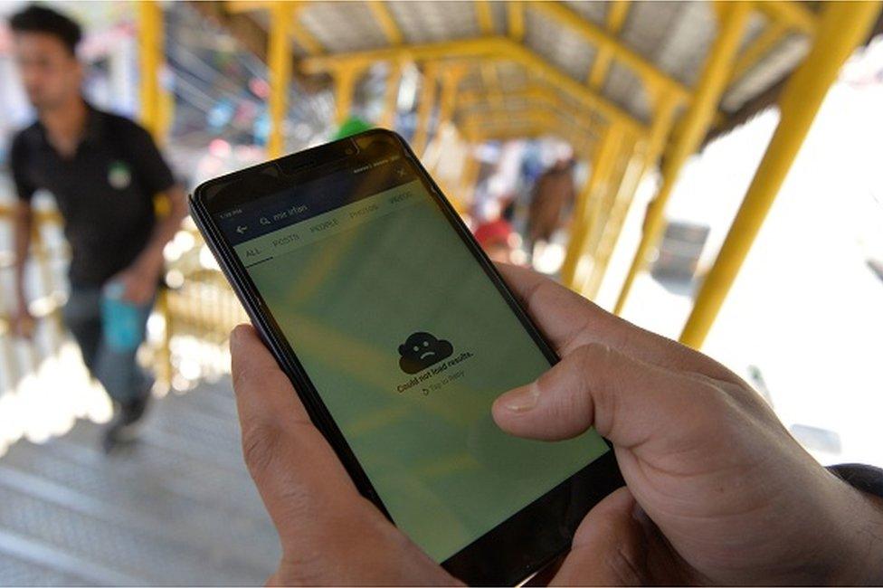 An Indian Kashmiri man browses blocked services on the internet on his mobile phone on a footbridge in Srinagar on April 27, 2017. -