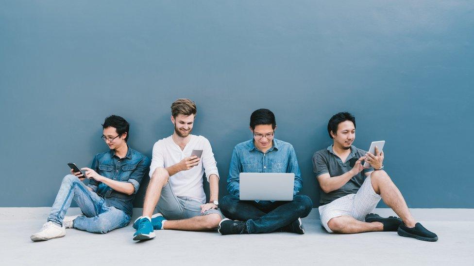 Four men use phones and a laptop