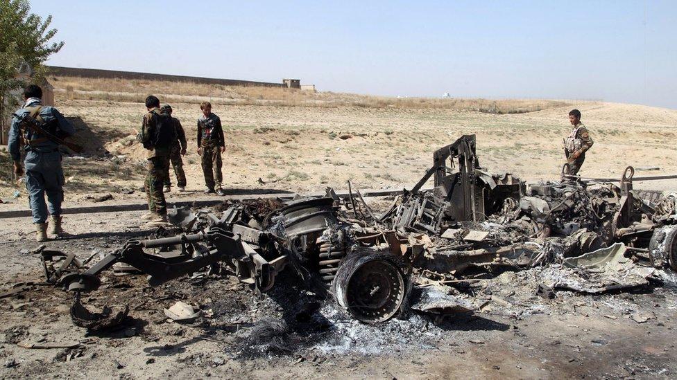 Afghan security personnel walk around a burnt out vehicle near Kunduz city, north of Kabul, Afghanistan, Thursday, Oct. 1, 2015