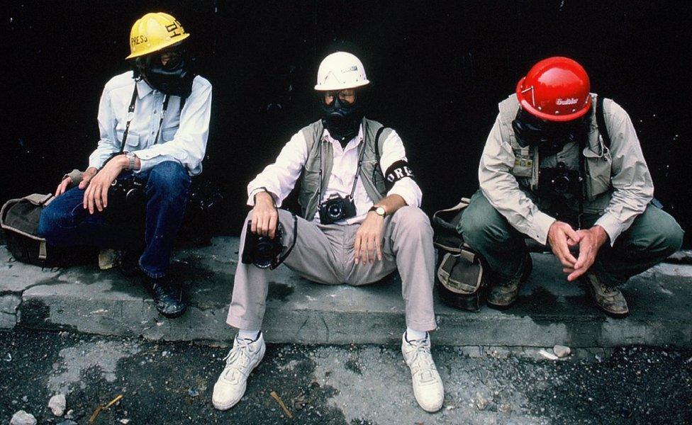 Charlie Cole sitting with two other men wearing gas masks and helmets