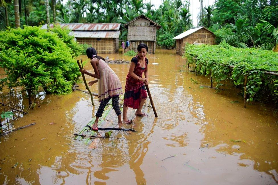 Girls row a makeshift raft past submerged houses at a flood-affected village in Assam's Karbi Anglong district.