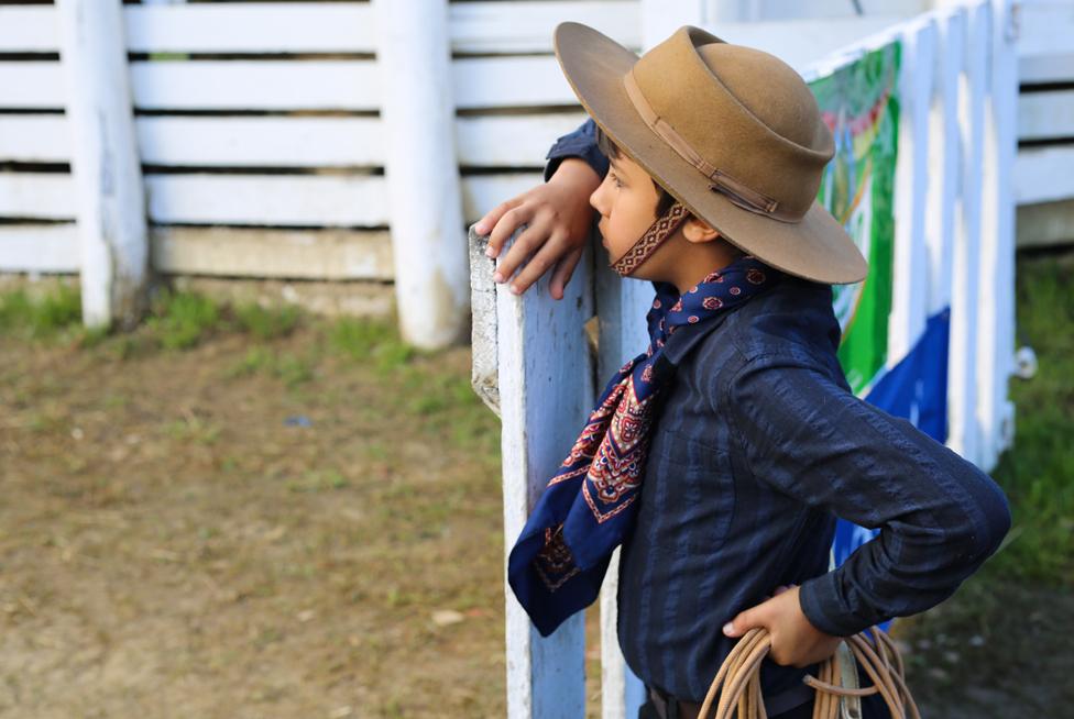 A young gaúcho watches a rodeo, lasso in hand