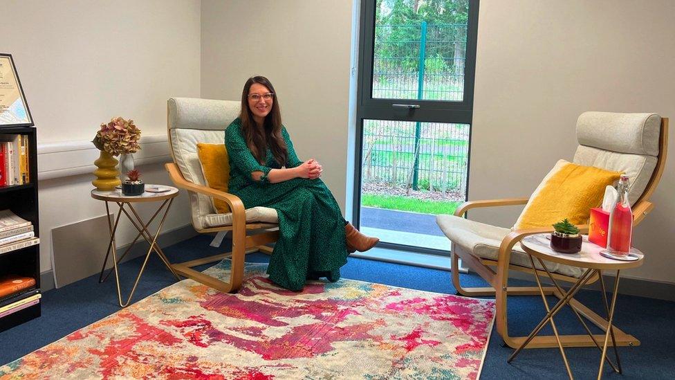 Anna McGuire. She is pictured in her rented office space, sitting on a chair and smiling at the camera