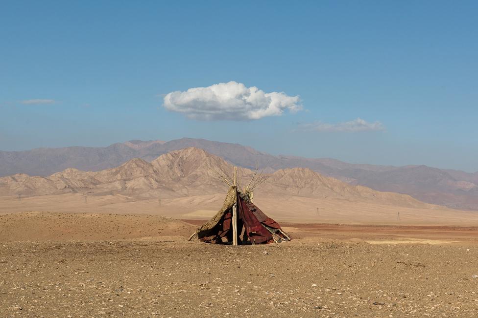 Tent in front of mountains, below a small white cloud in the sky