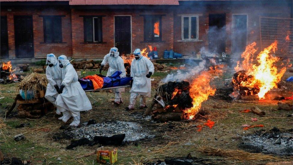 Nepalese soldiers in PPE carry a body away at a crematorium