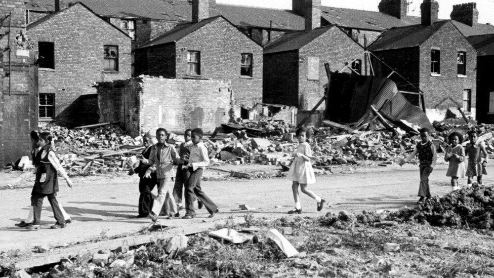 Children walk past houses destroyed in the slum clearance