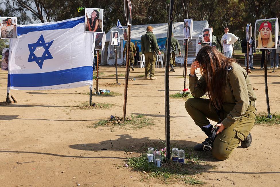 An Israeli soldier sits among pictures of people taken captive or killed by Hamas militants during the Supernova music festival on October 7, at the site where the deadly incident took place near Kibbutz Reim in southern Israel, on January 5, 2024.