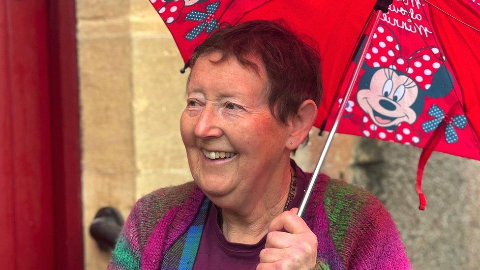 Annie standing in front of her front door with an umbrella