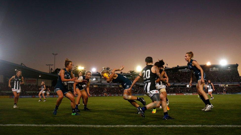 A woman holding a football evades players in a dramatic shot