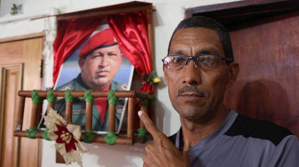 Marcos Lobos points to a shrine to the late president, Hugo Chávez, in his home