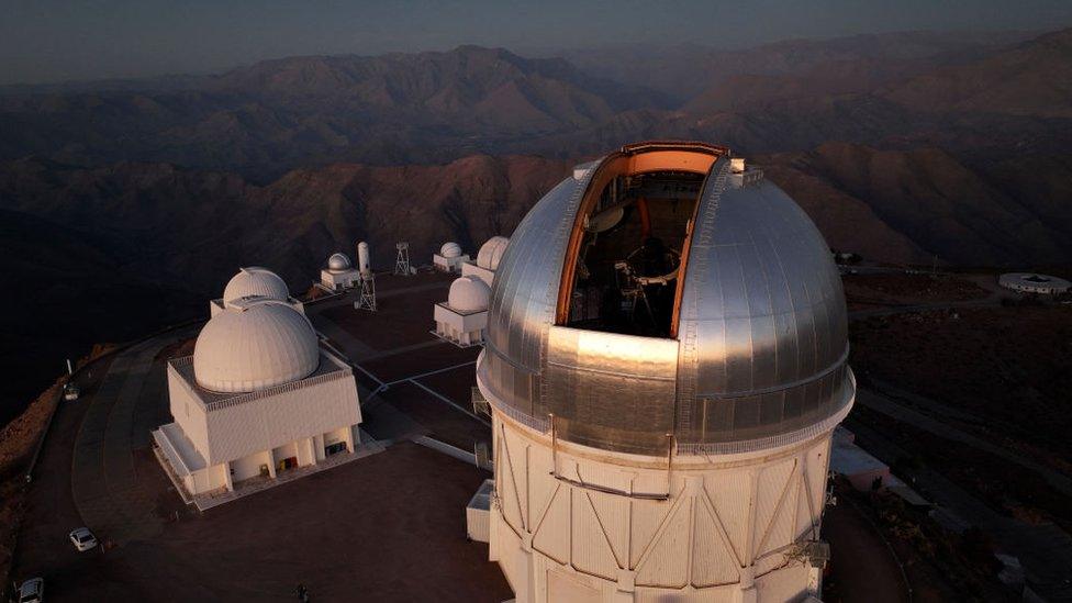 A photo showing an observatory - domed buildings on a hilltop in Chile.