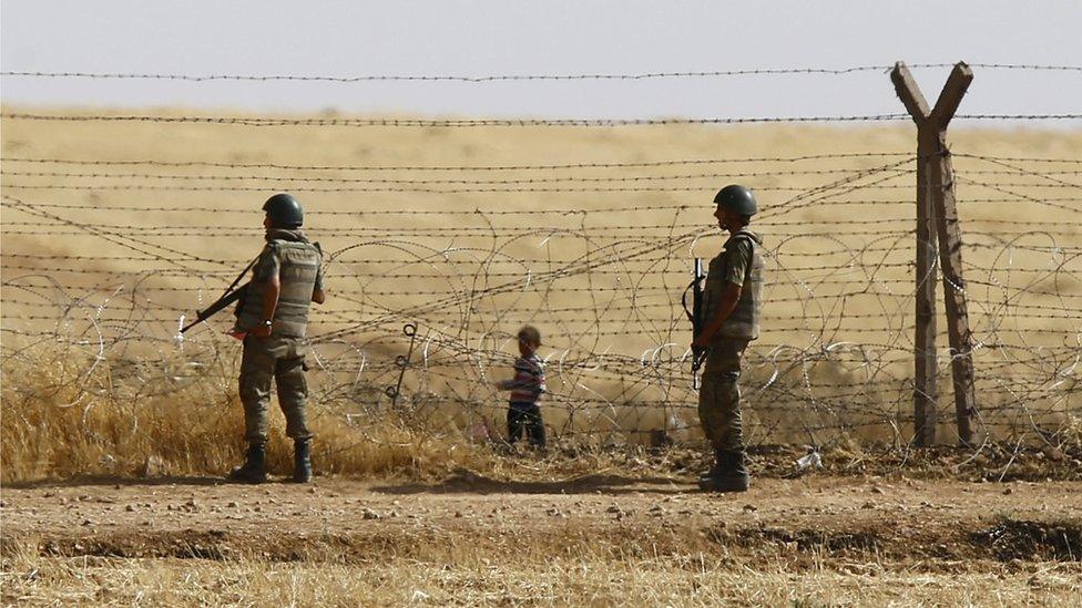 Turkish soldiers stand guard as a Syrian refugee boy waits behind the border fences to cross into Turkey on the Turkish-Syrian border on 5 June