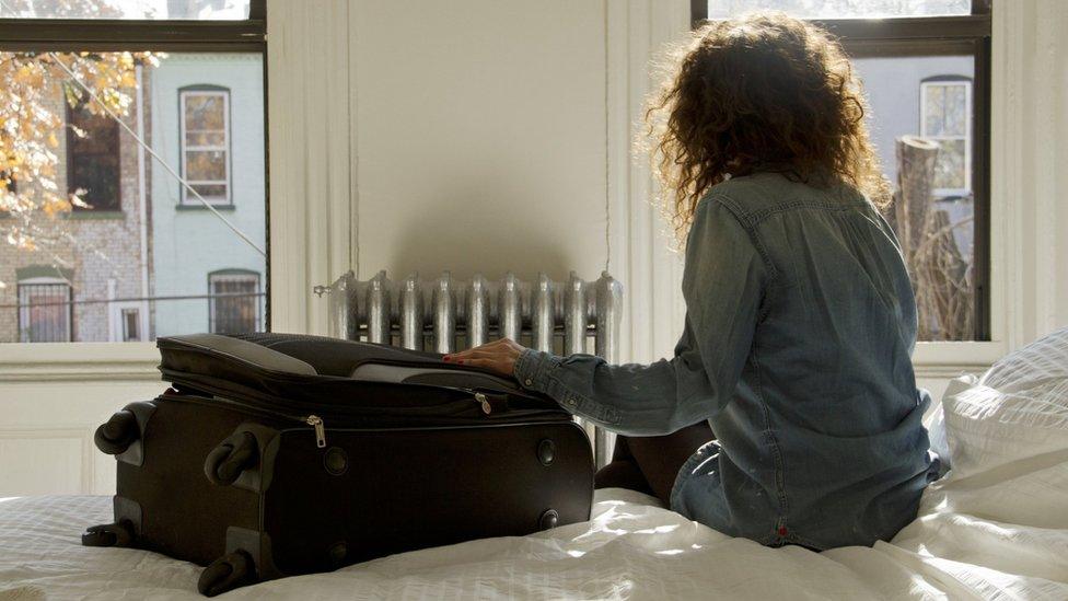 Female traveller sat on an Airbnb bed.