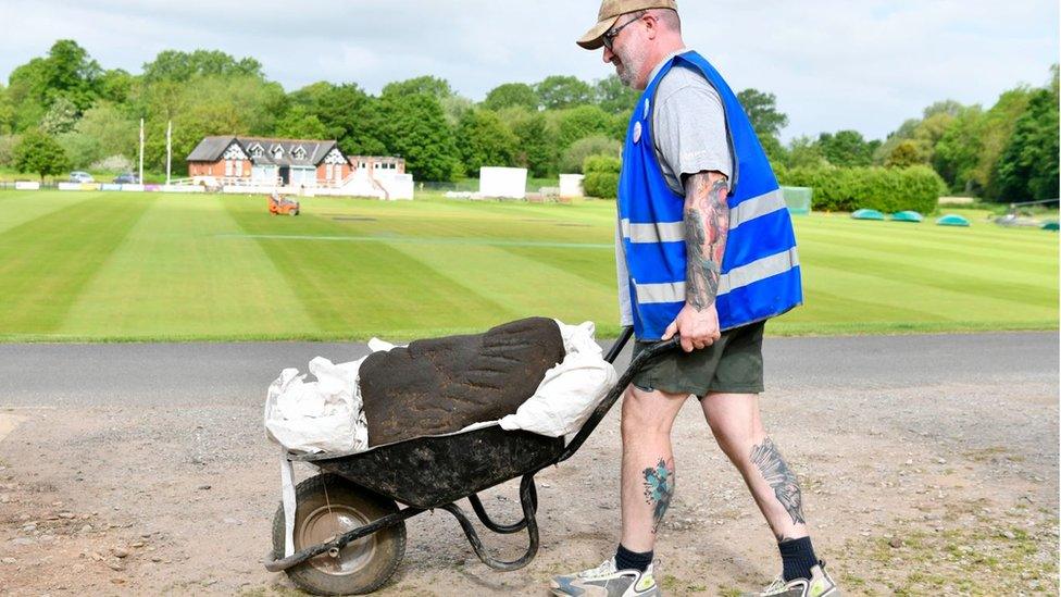 Man pushes a large Roman sculpted head in a wheelbarrow