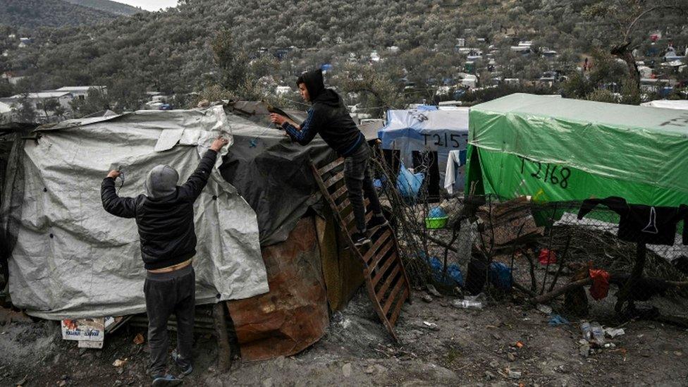 Two young men cover their shelter with plastic sheets at a makeshift camp in Moria, in the island of Lesbos, 21 January 2020