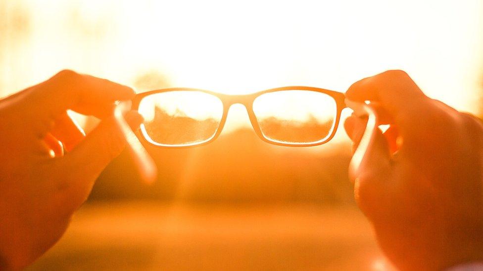 A person holding glasses against the sun