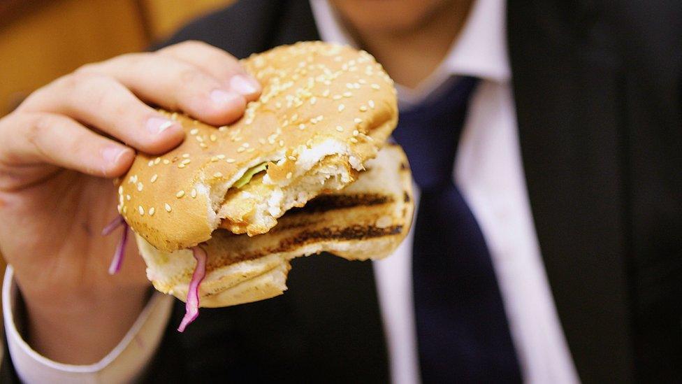 A school pupil eats a burger for lunch which was brought from a fast food shop near his school in London, 5 October 2005