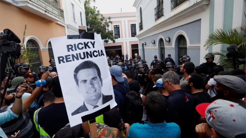 Protesters holding sign calling for resignation