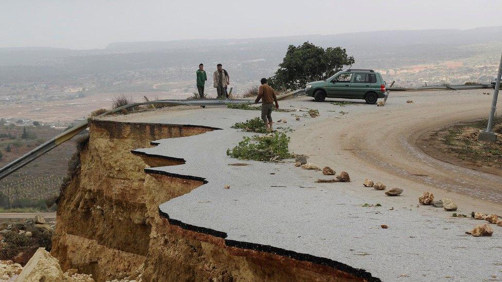 People stand in a damaged road as a powerful storm and heavy rainfall flooded hit Shahhat city, Libya, September 11, 2023