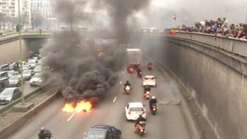 traffic on an eight-lane road, driving around a huge fire in the centre