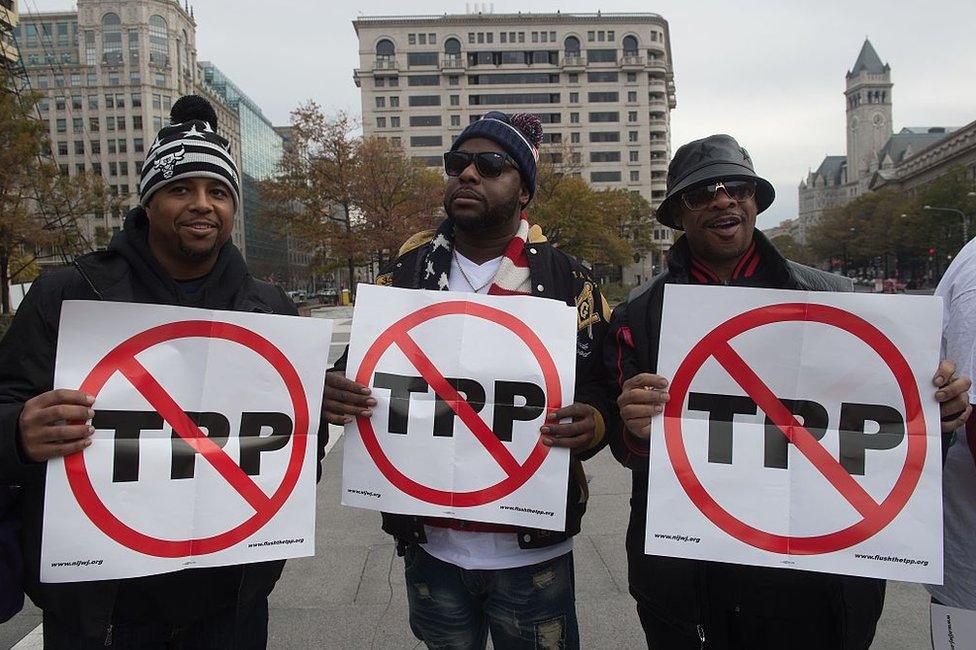 People hold signs as they demonstrate against the Trans-Pacific Partnership (TPP) trade agreement in Washington, DC, on 14 November 2016