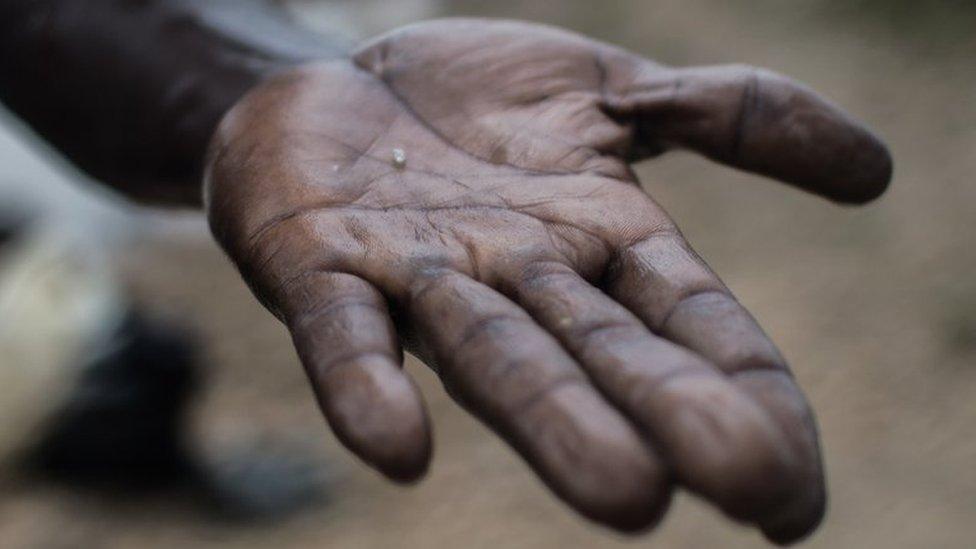 A man holds out a small diamond