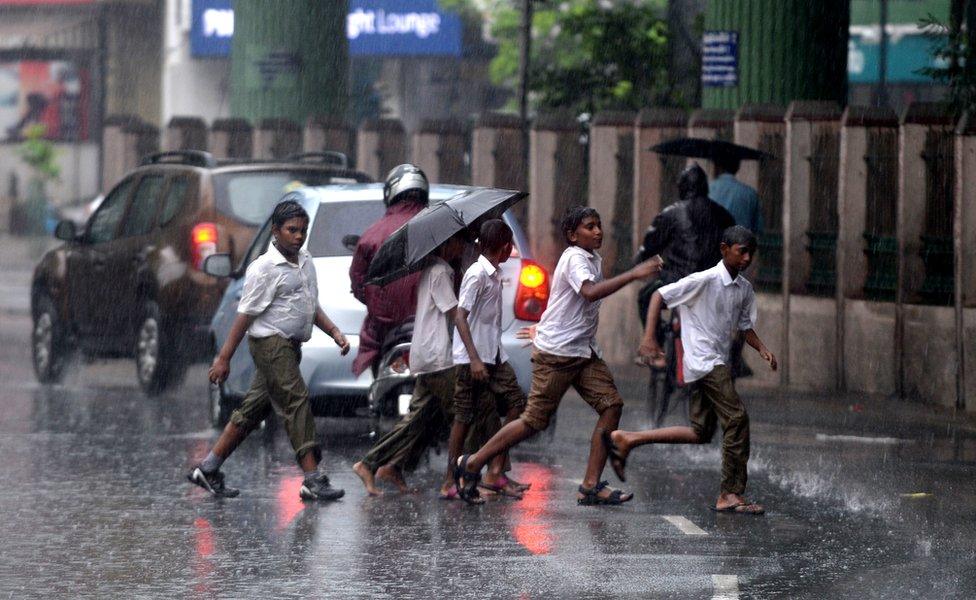 Indian school students cross the street under monsoon rains in Chennai