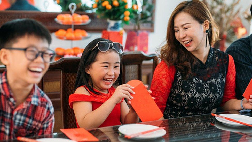 Chinese girl opening a red parcel at a family dinner during Chinese New Year