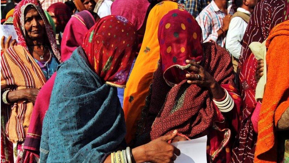 Women check their documents as they queue outside a bank to exchange and deposit their old high denomination banknotes in Gagwana village in the desert Indian state of Rajasthan