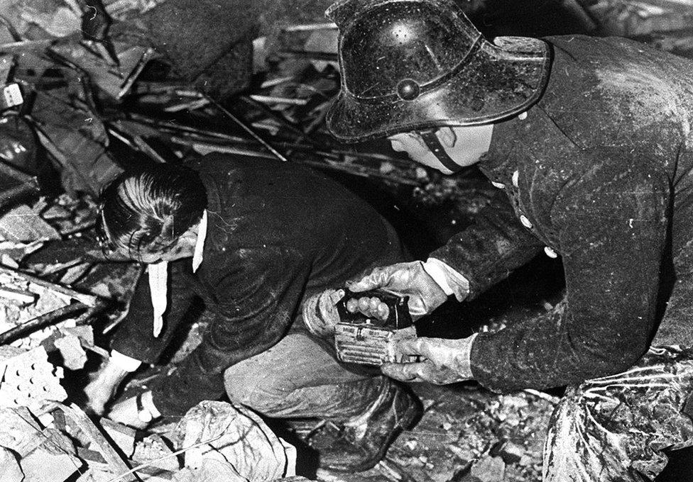 A firefighter holds a torch while a man searches through the rubble of McGurk's bar