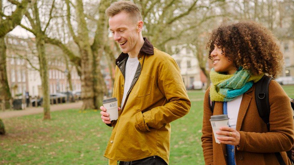 A man and woman walking holding a returnable coffee cup