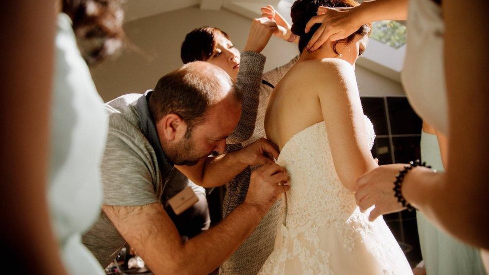 Syrian refugee Ibrahim Halil Dudu fixes the broken zip on Jo Du's wedding dress