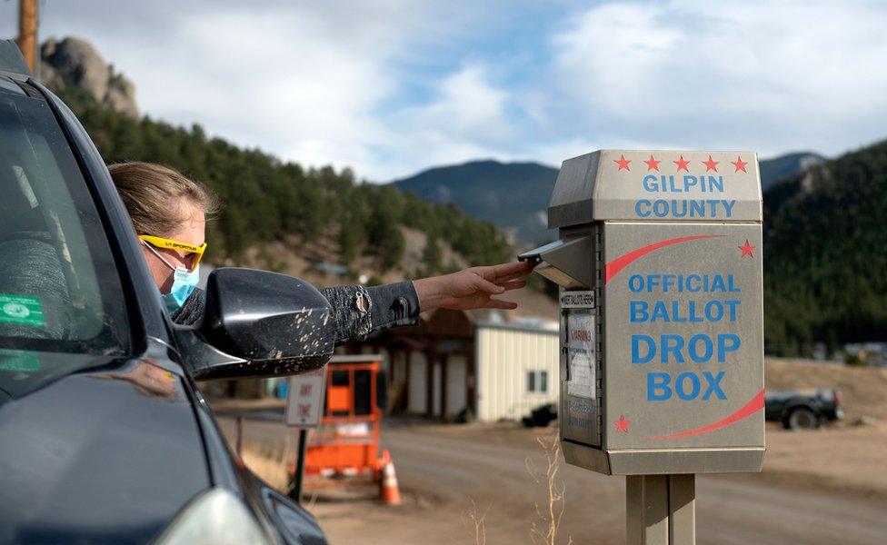 A voter leans out her car to deliver her ballot into a ballot box