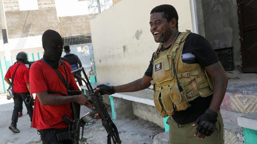 Former police officer Jimmy "Barbecue" Cherizier, leader of the 'G9' gang alliance, receives his weapon from a gang member after a press conference in Delmas 6, Port-au-Prince, Haiti March 5, 2024