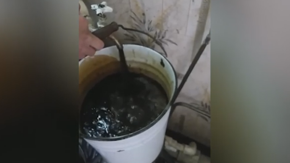 A still from a smartphone video showing oil pouring from an indoor tap into a bucket