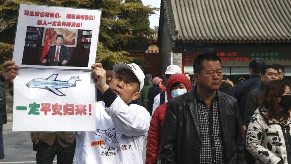 A relative (left) of an MH370 passenger holds a sign urging President Xi to help find out what exactly happened in the disaster during a protest outside the Yonghegong Lama Temple in Beijing (08 March 2016)