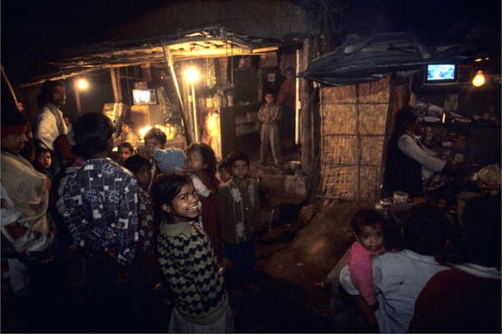 People in the streets gather around shops with televisions at night in January of 1999 in the slums of New Delhi, India.