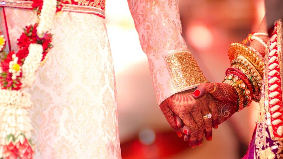 Groom holding henna decorated hand of bride (generic image)