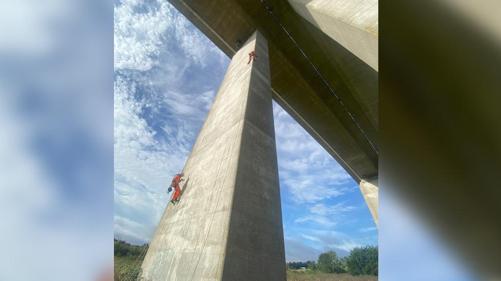 A photograph looking up at one of the pillars, with two contractors abseiling.