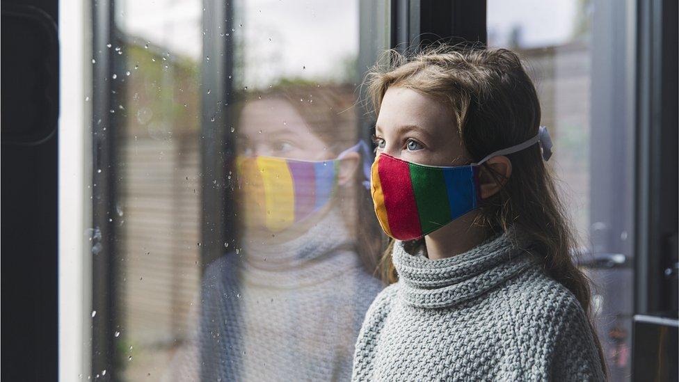 A young girl wearing a mask looks through a window