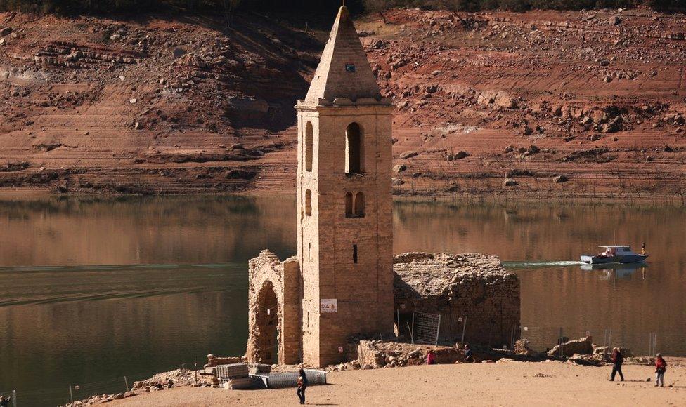 Tourists walk while fishermen collect fish from the Sau reservoir in the northern Spanish region of Catalonia