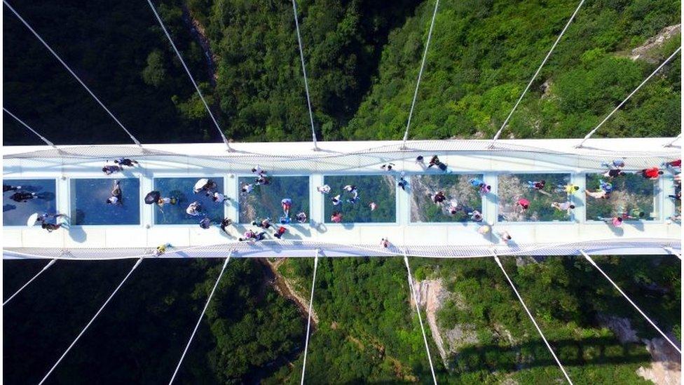 Visitors walk across a glass-floor suspension bridge in Zhangjiajie in southern China's Hunan Province Saturday, Aug. 20, 2016