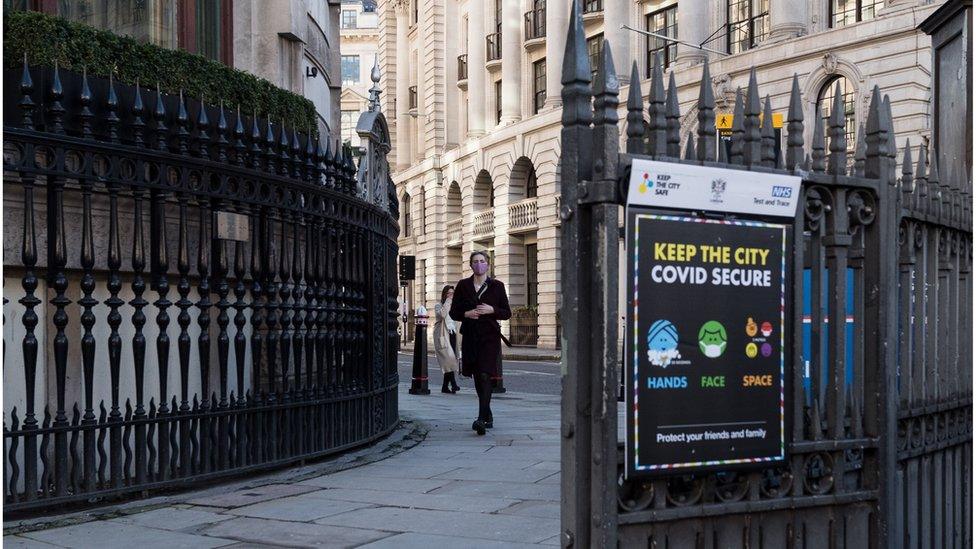 A person in a mask walks past a 'Keep the City Covid secure' sign