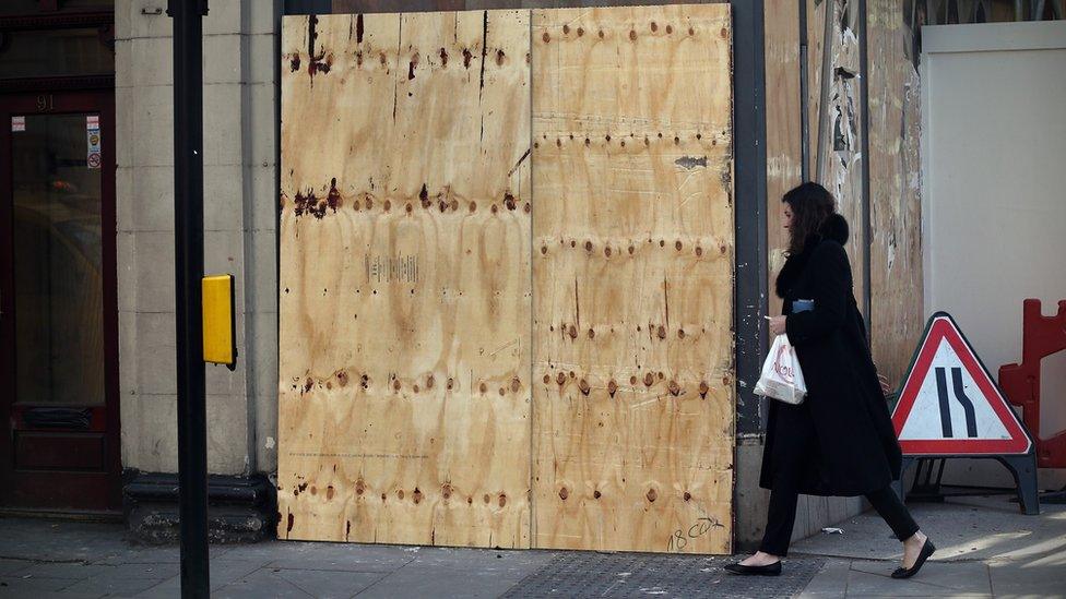 A woman walks past plywood hoarding covering a Banksy artwork opposite the French embassy