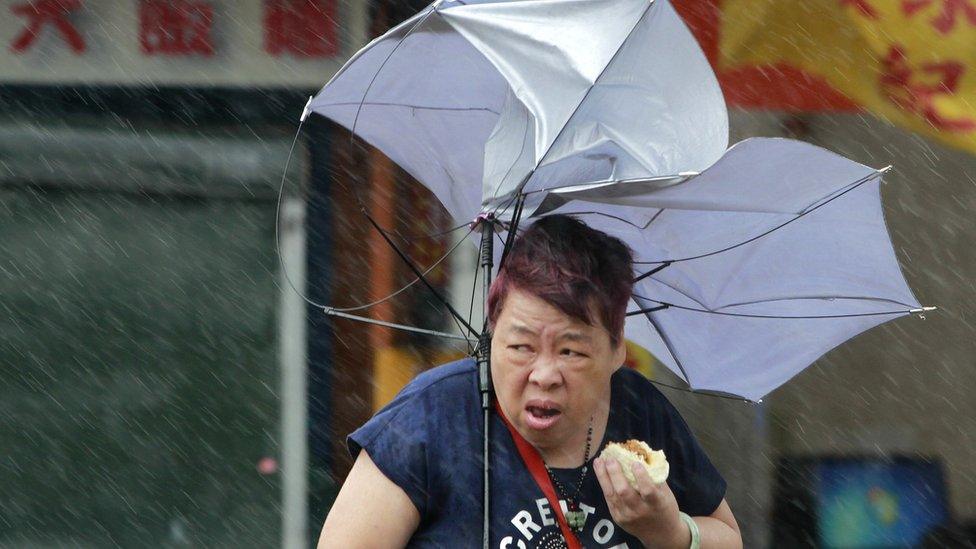 Woman eats a pork bun and struggles with her umbrella against powerful gusts of wind generated by Typhoon Megi in Taipei, Taiwan