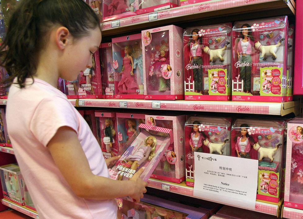 Girl looks at Barbie on toy shop shelf